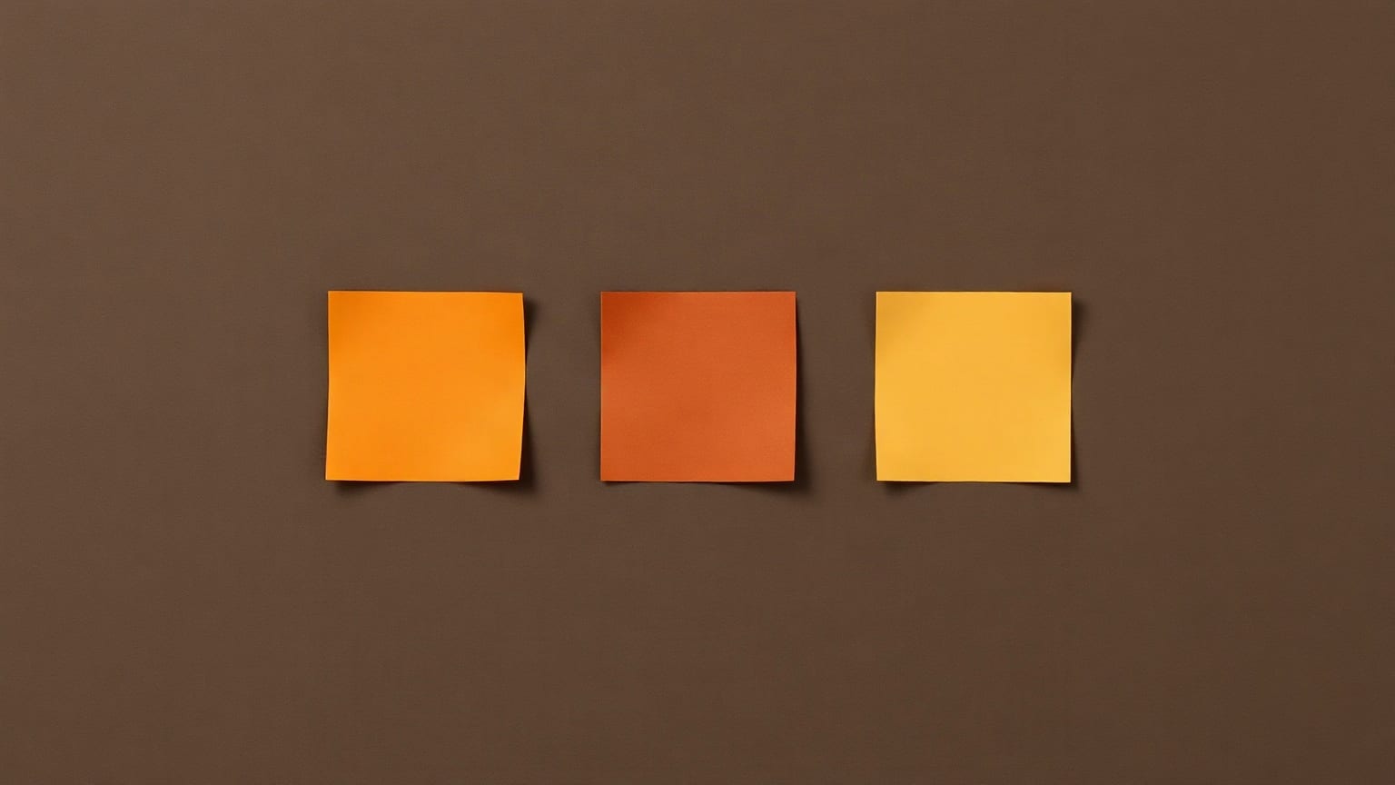 Three square sheets of paper hung in a row on a dark brown ground, one amber, one russet, one yellow