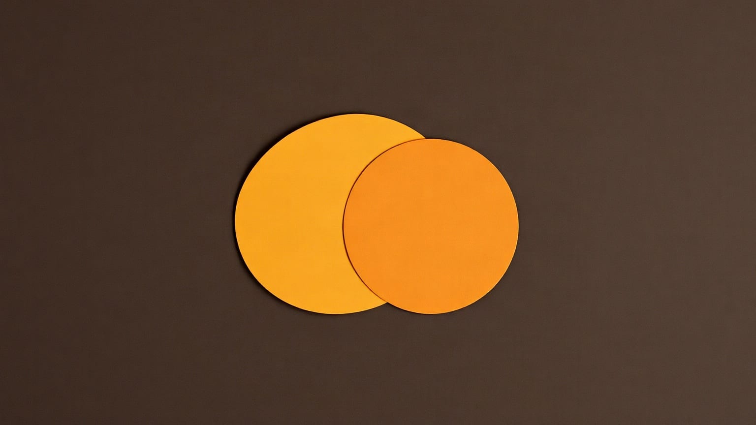Two identical amber paper circles of the same size overlapping at the centre of a dark brown ground